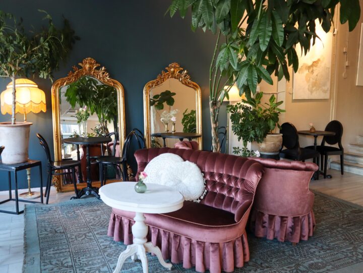 Relove Second hand & Café Töölön sisätilat. Valkoinen pöytä, punertava tuoli ja sisäkasveja. Taustalla isot peilit seinää vasten.