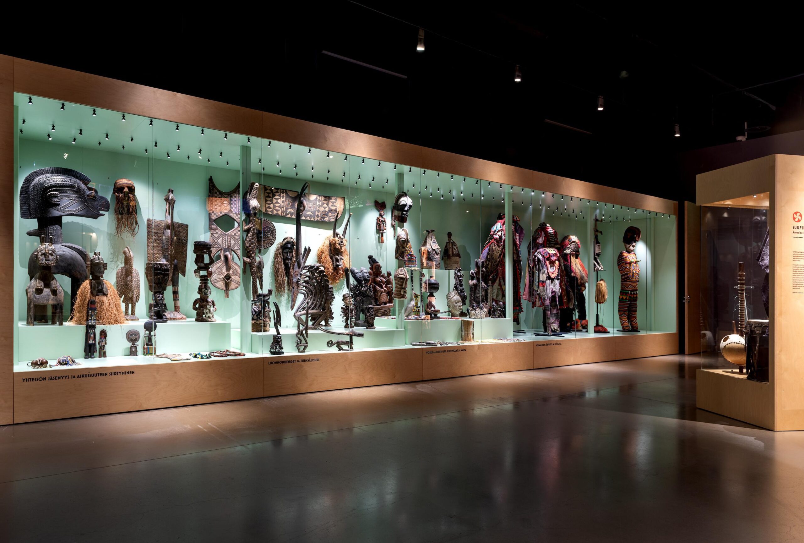 Länsi-afrikkalaisia esineitä, naamioita, soittimia ja pukuja lasivitriinissä, museotilassa.