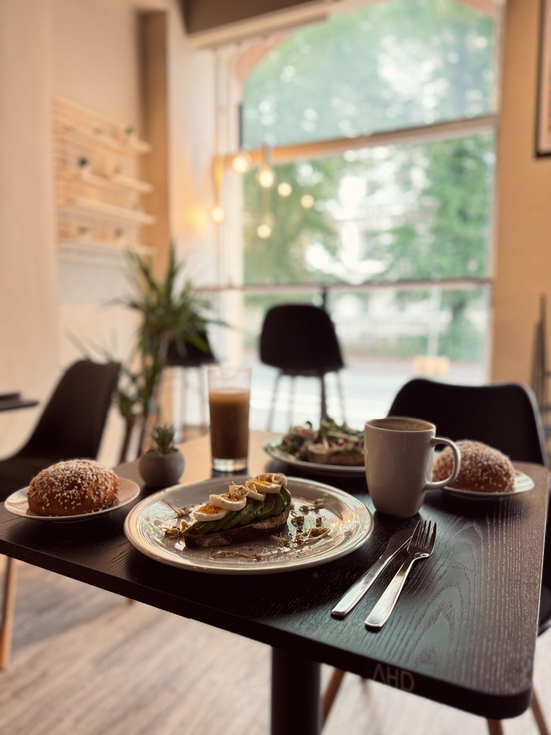 Tintin The Bakery & The Cafén sisätilat. Pöydällä on kahvia, kakkupala ja leivonnaisia. Taustalla isot ikkunat ulospäin.