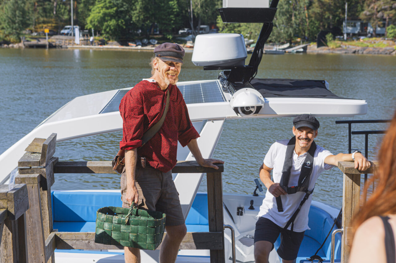 Two men on a boat deck, one holding a green basket, smiling