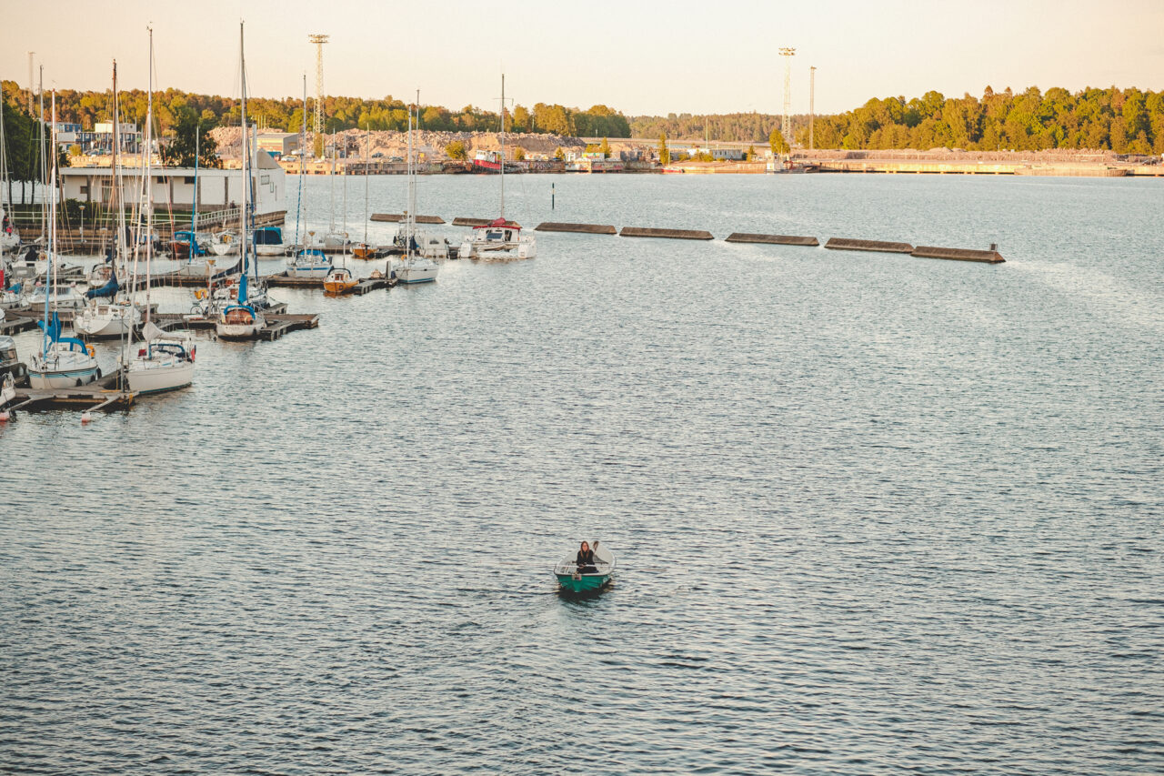 Man in small boat on calm water with sailboats docked in background