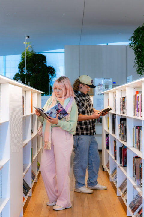Two people reading books in a modern library aisle.