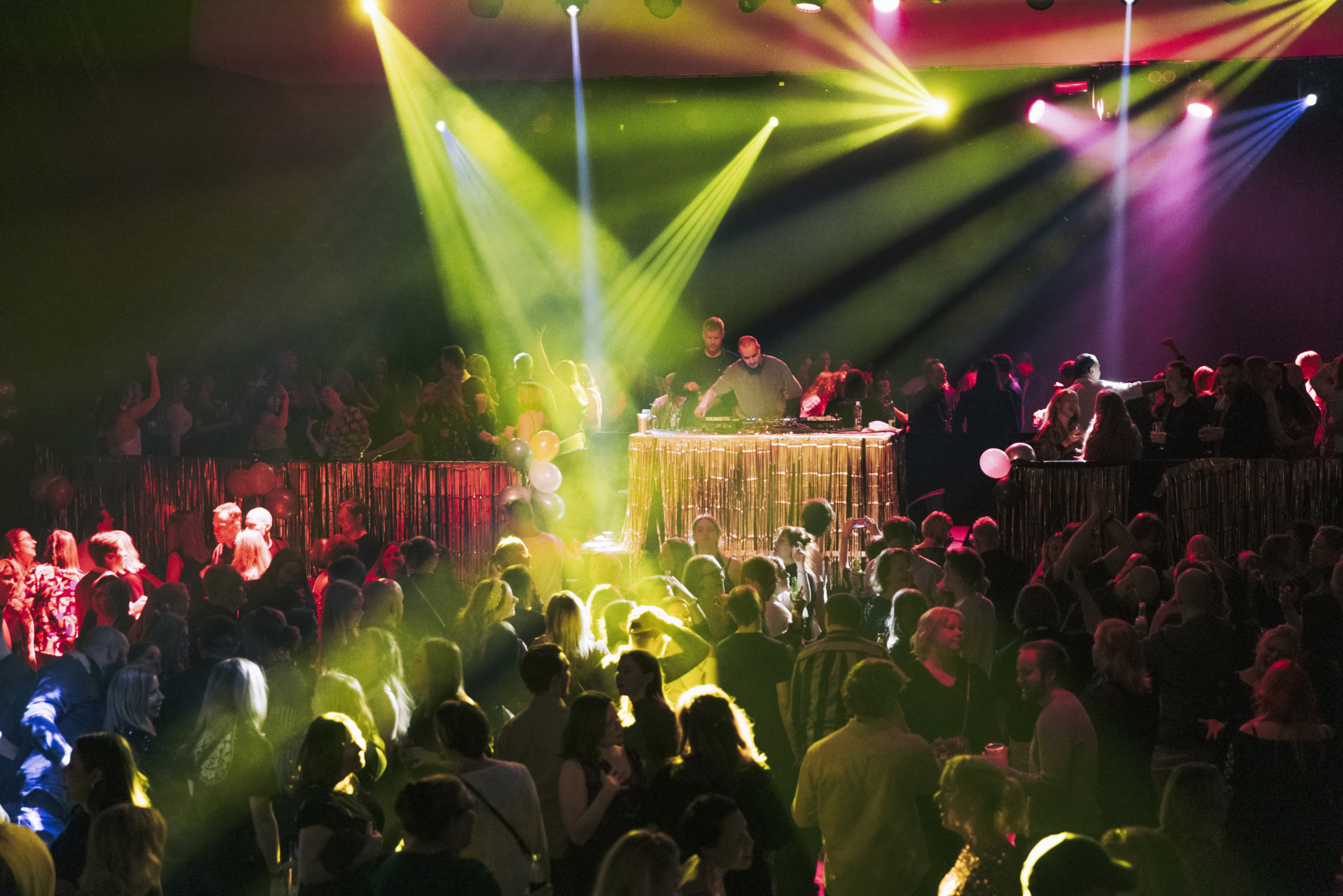 Crowd dancing under green and purple stage lights at a concert