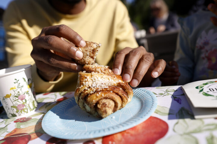 Person's hands breaking a cinnamon bun with pearl sugar on a blue plate
