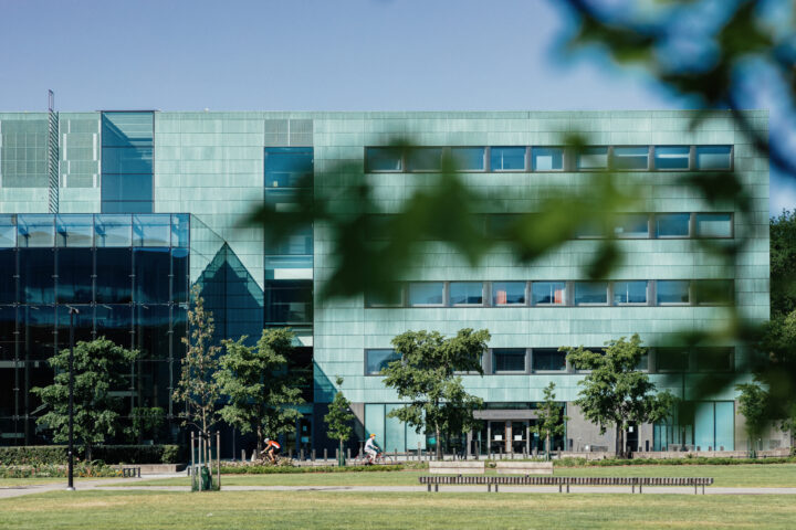 Modern green building with glass facade, trees, and cyclists