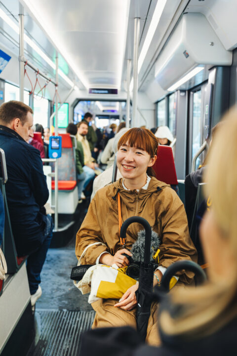 Young woman smiling on a tram, holding a yellow bag and an umbrella.
