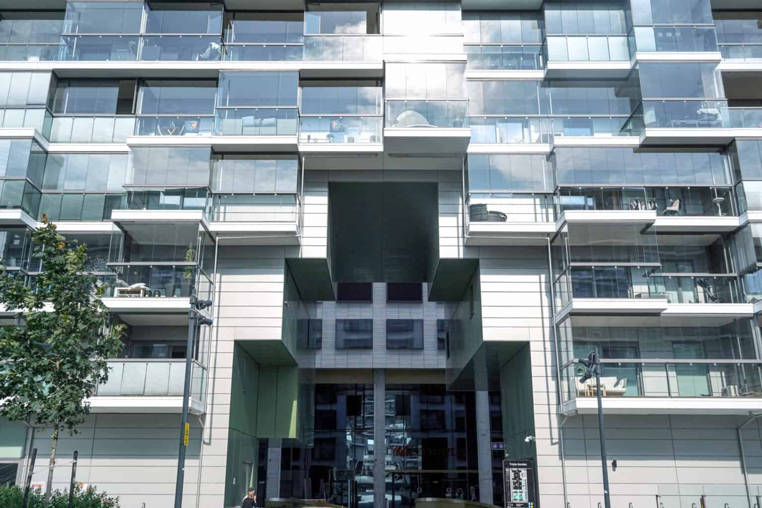 Modern glass apartment building with balconies and a tree in front.