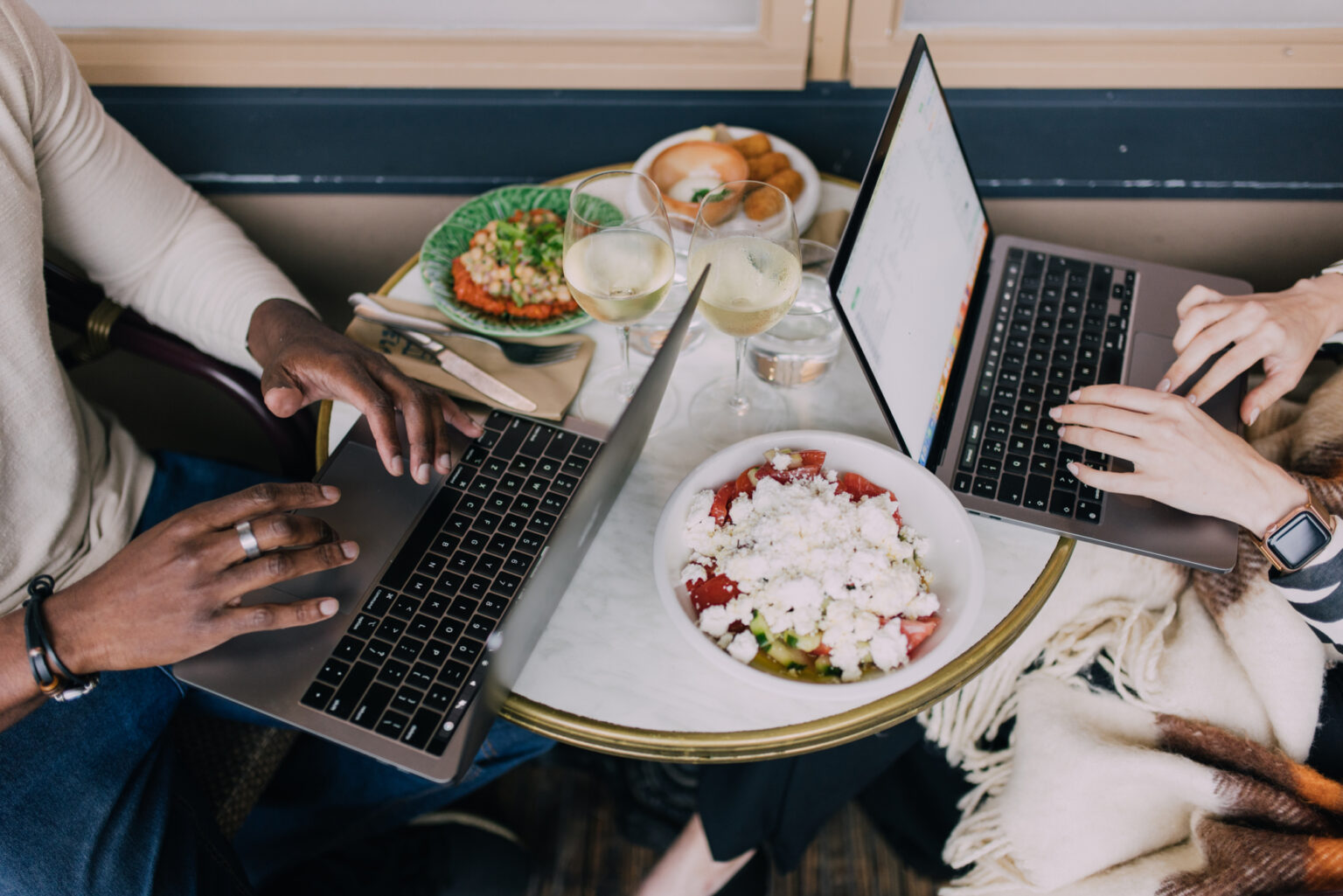 Two people working on laptops at a table with food and drinks