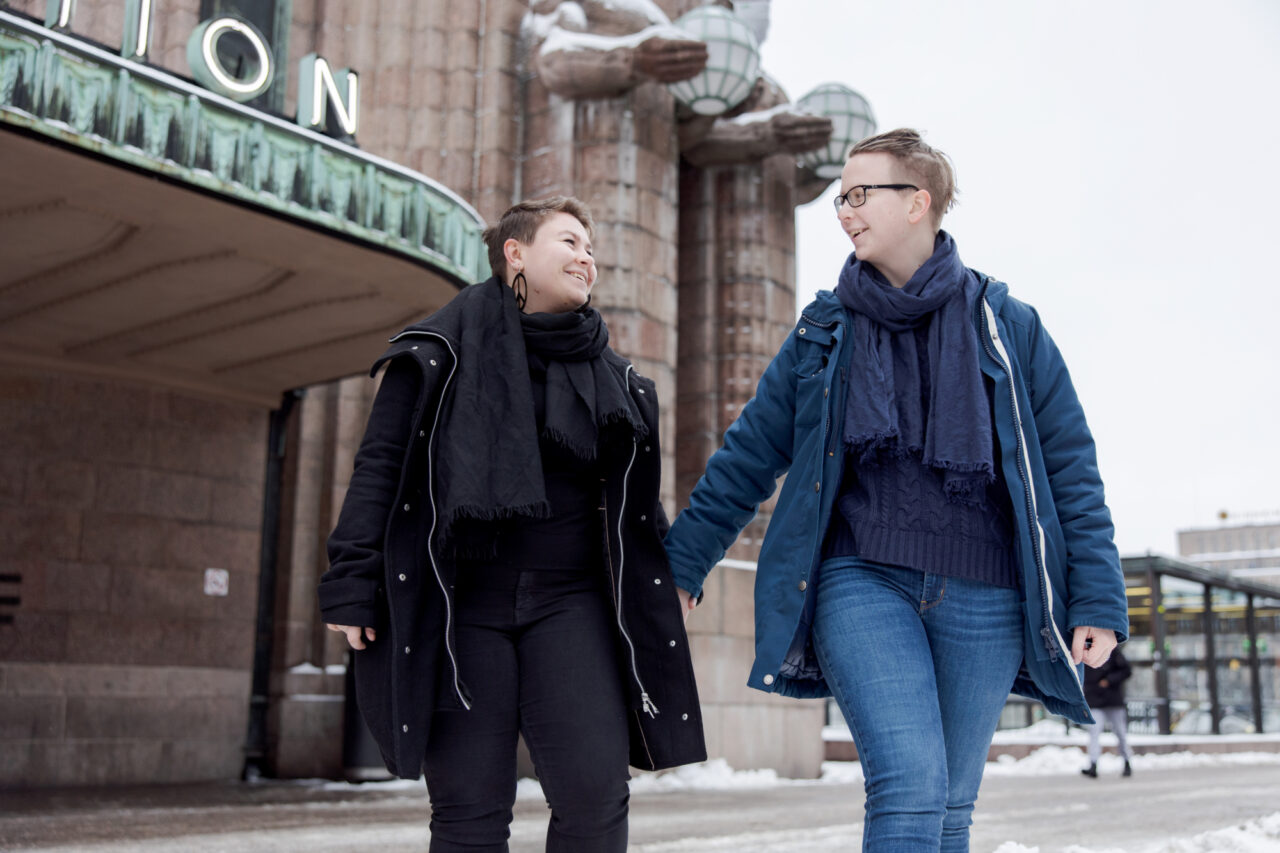 A couple walking in front of the Helsinki Railway station holding hands.