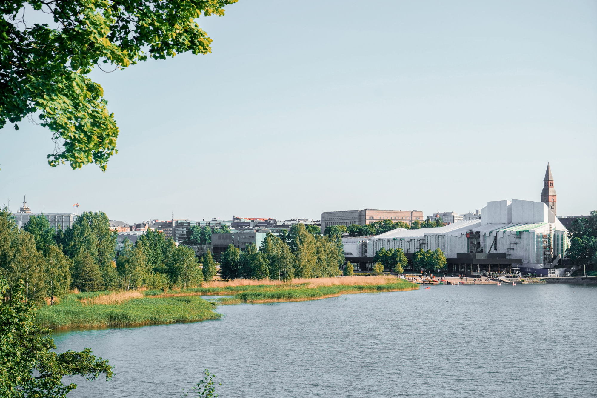 Helsinki cityscape with modern buildings and a lake, viewed from a park.
