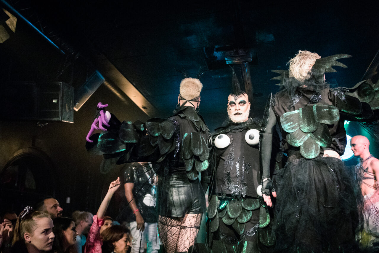 a group of people wearing costumes walking the runway at a drag show