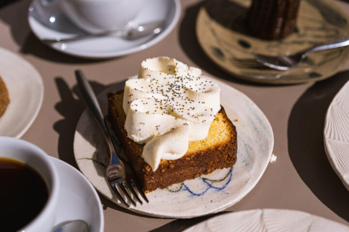 Slice of pound cake with whipped cream and poppy seeds, served with coffee.
