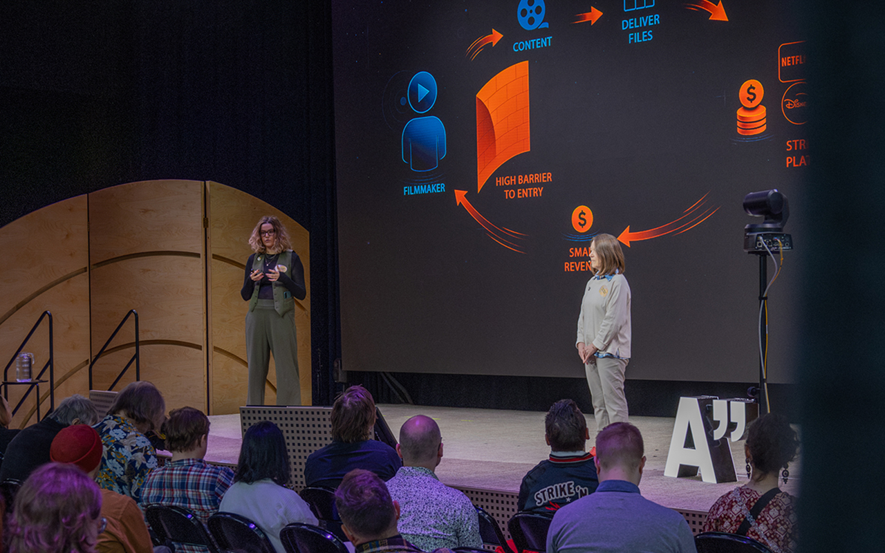 The founders of Cyon.media, Lotta Stenroos and Tracie Mitchell, speaking on an event stage about their startup in Helsinki.