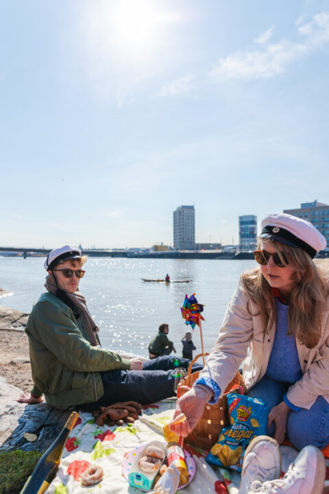 Two graduates in caps and gowns enjoying a picnic by the water