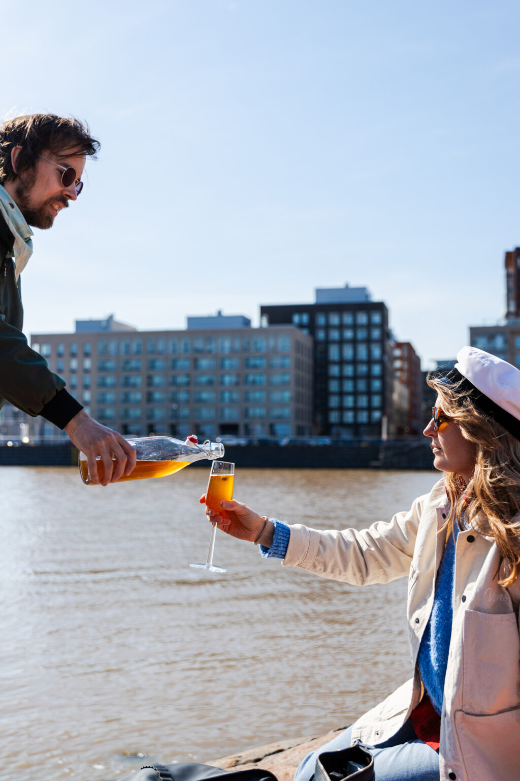 Man pours drink for woman wearing graduation cap by water