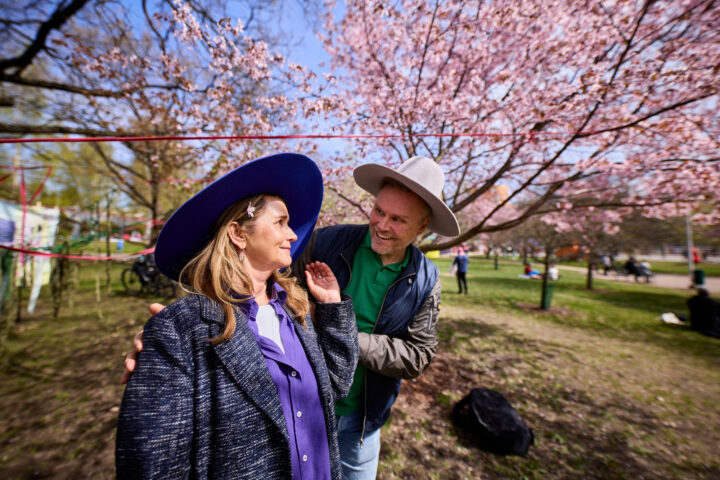 Couple in hats smiling under cherry blossoms in a park