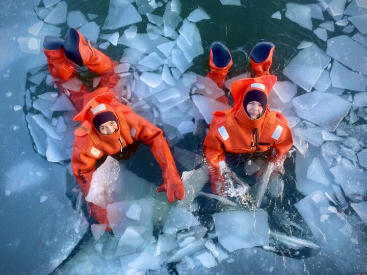 Two people in orange survival suits floating in icy water.