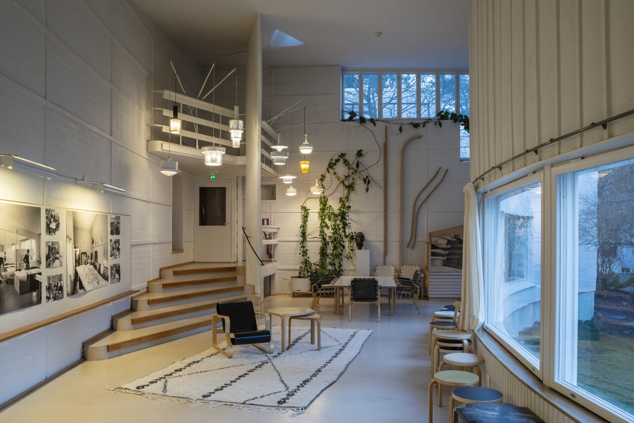 Modern minimalist living room with white walls, wooden stairs, and large windows.