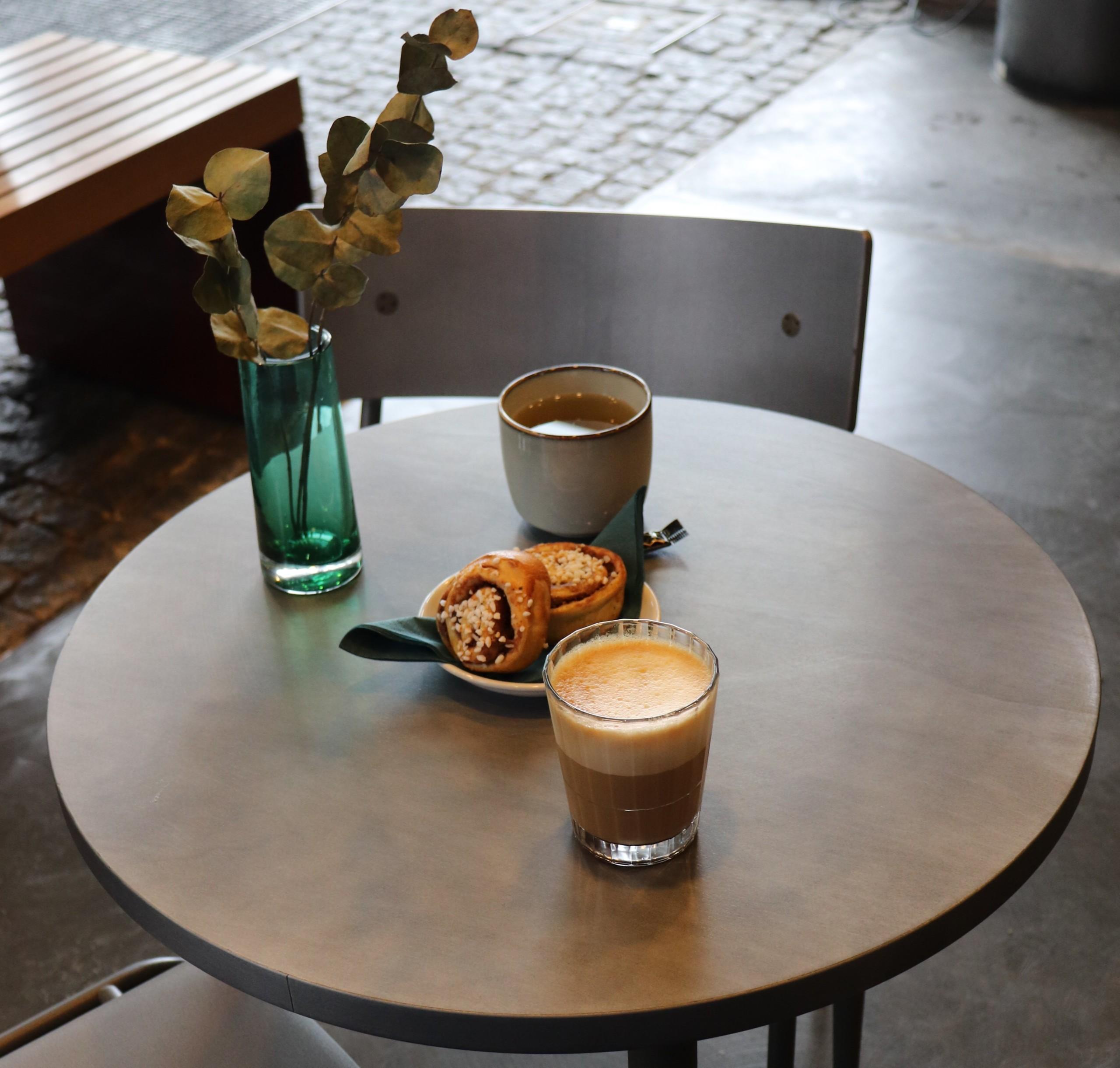 Suomenlinna Centre Café, photographed from the inside. On the table there's coffee, tea, cinnamon roll and flowers.