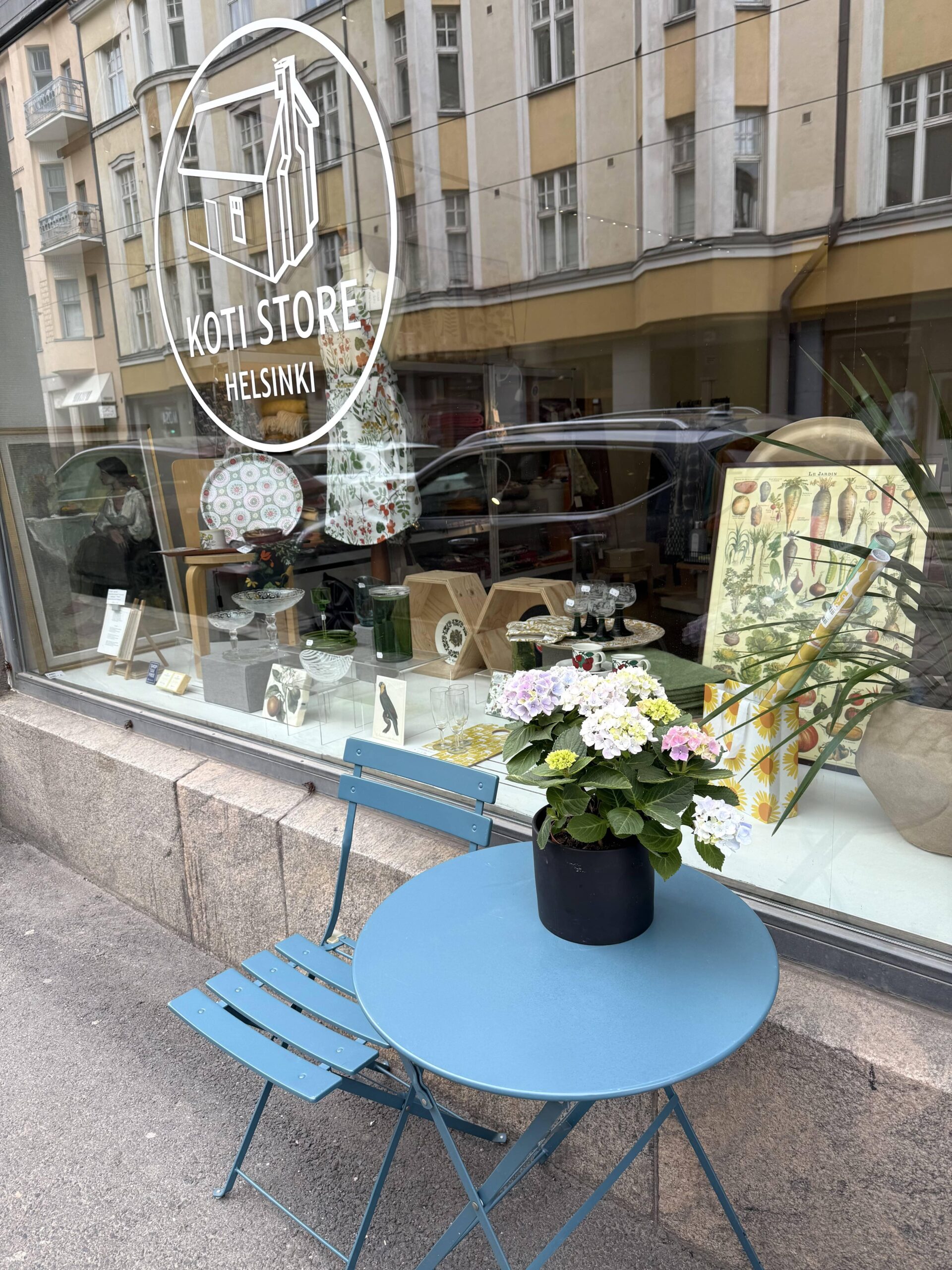 Koti Store Helsinki, the shop from the outside. In front of the store, there's a small blue table with flowers on top of it.