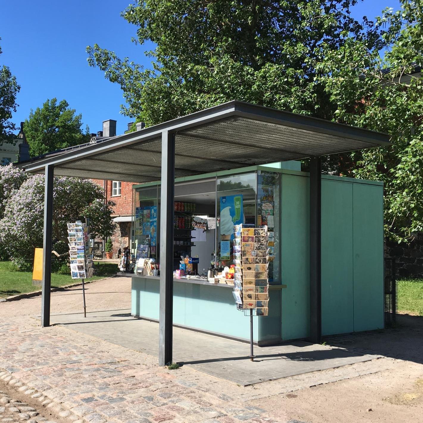 Artillerivikens kiosk, fotograferad utifrån. Bakom kiosken syns träd, och en byggnad i röd tegel.