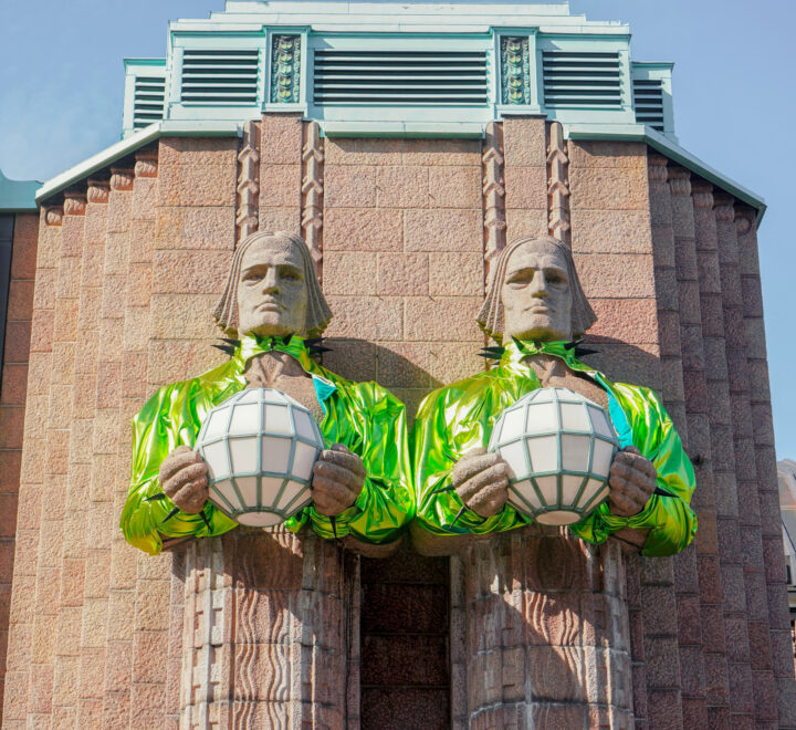 Two stone statues holding globes, dressed in shiny green jackets, on a brick building.