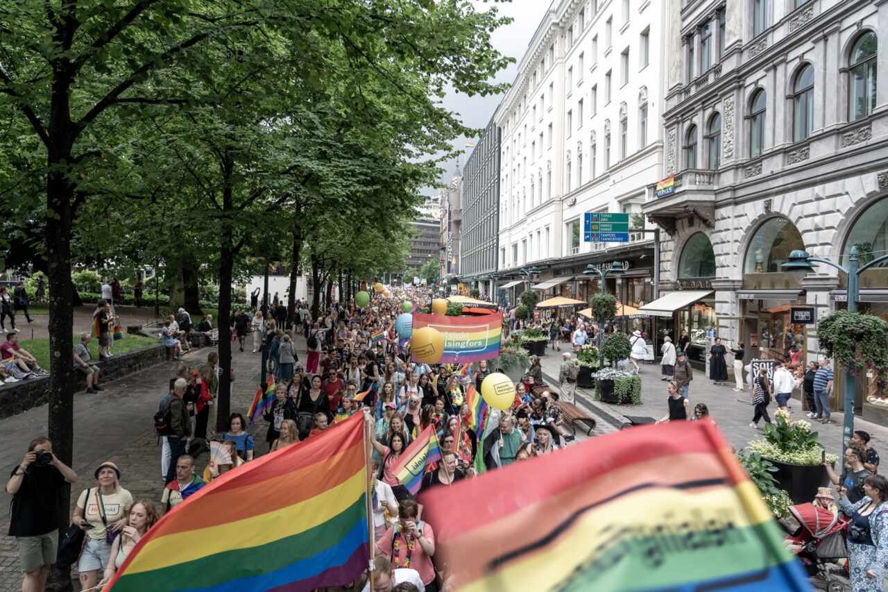 a group of people walking down a street with rainbow flags in support of LGBTQ+ rights in Helsinki 