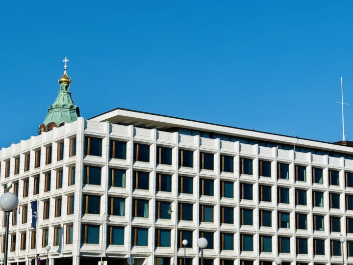 Modern white office building with a green dome and cross against a clear blue sky.
