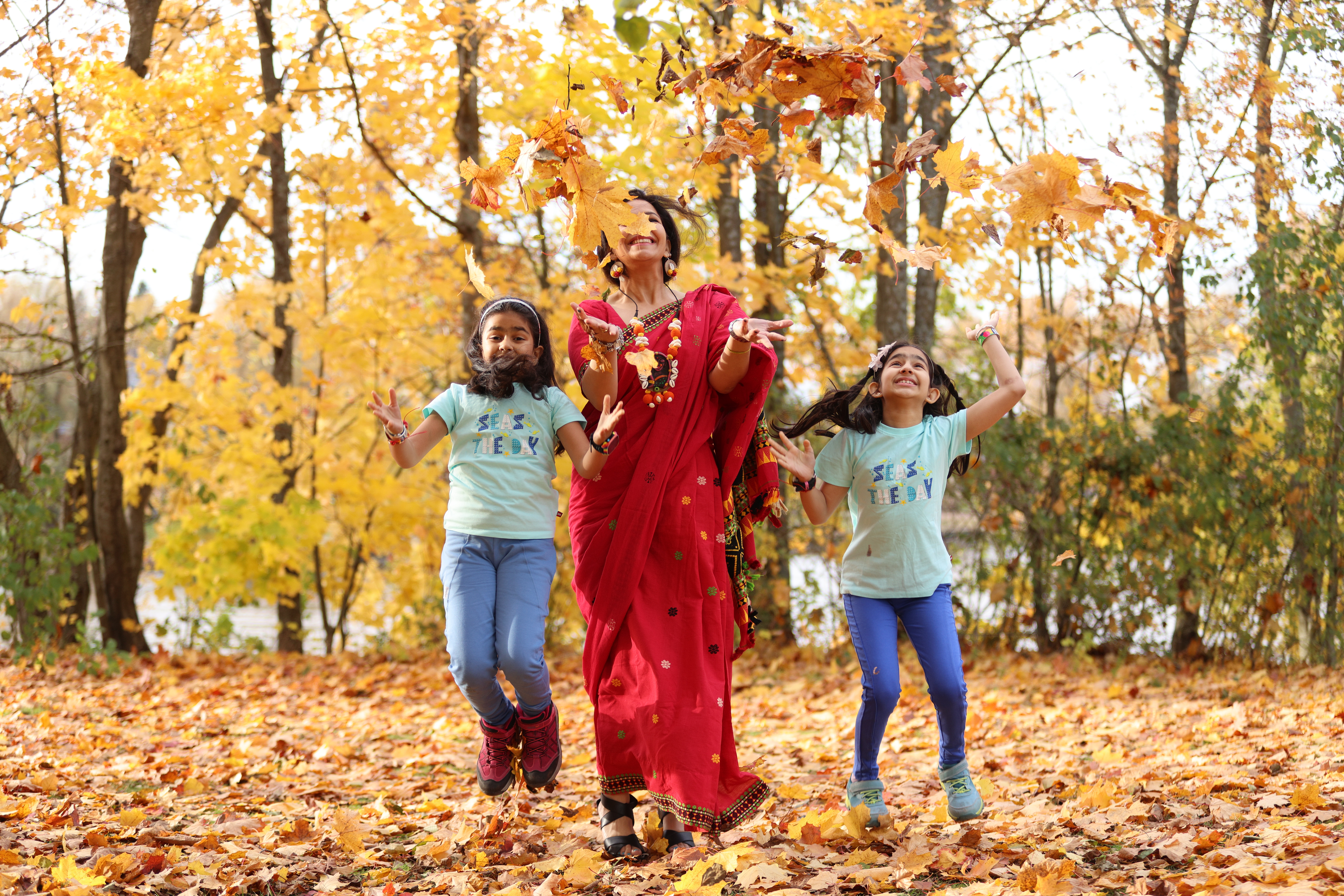 A woman and two girls playing with autumn leaves in a Helsinkian park.