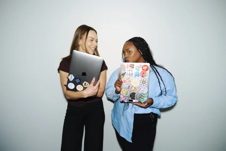 Two women holding laptops with stickers.