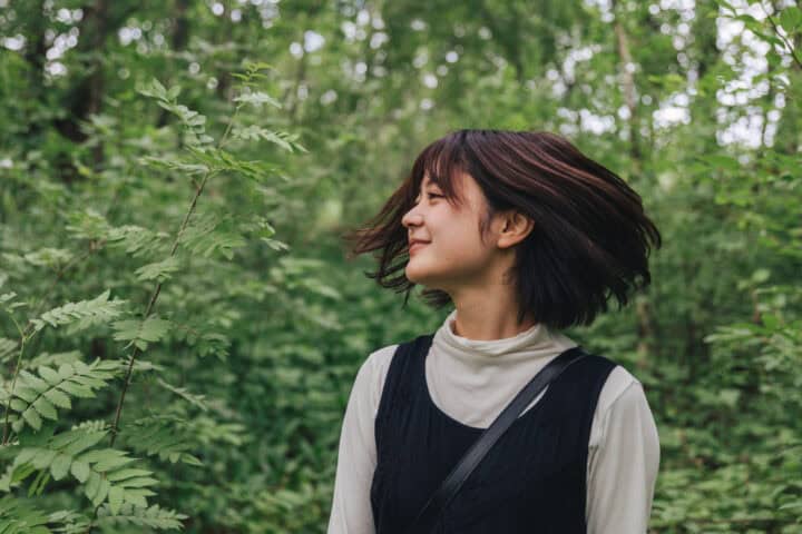 Young woman with short dark hair flipping her hair in a lush green forest.
