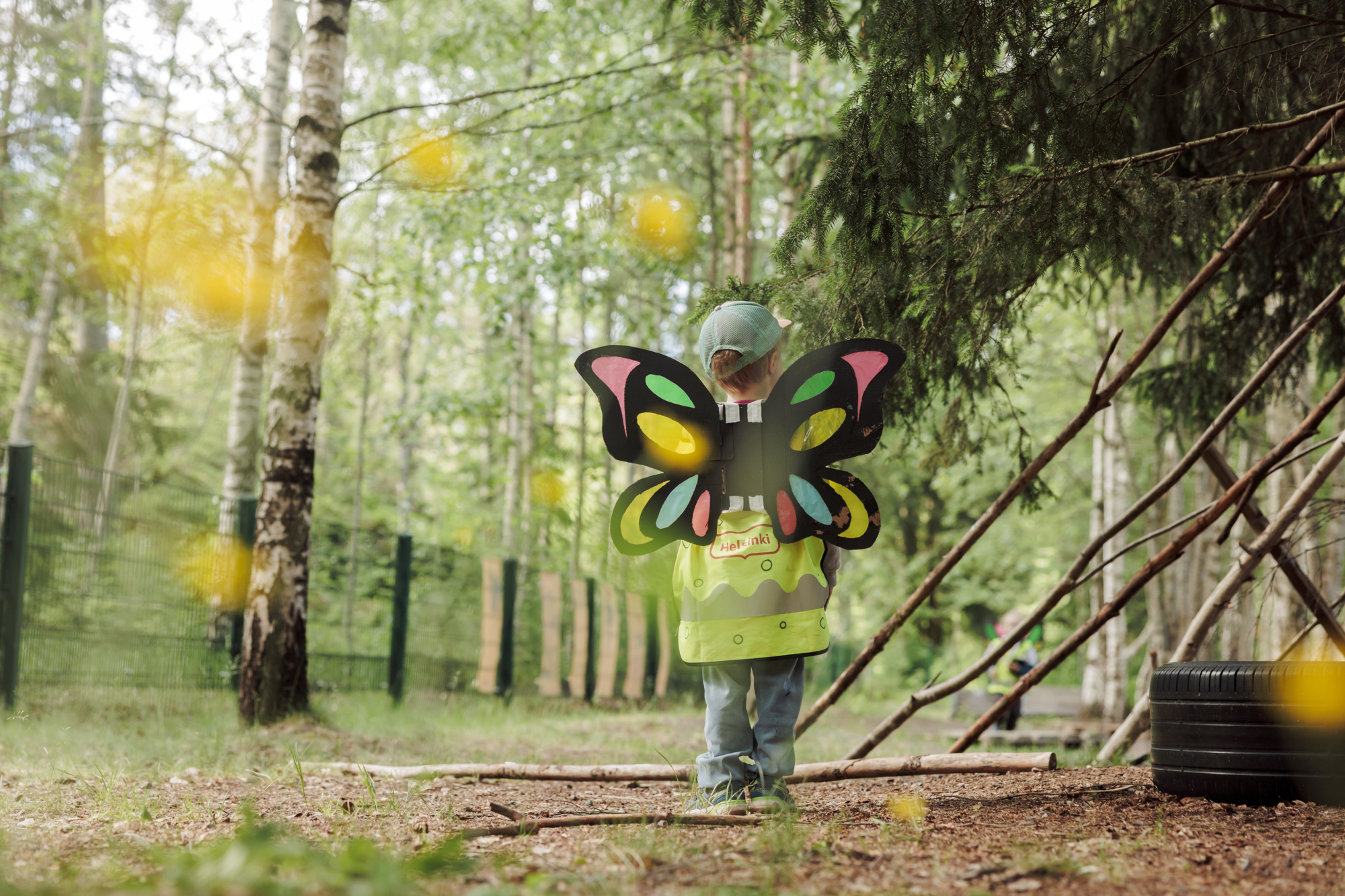 Child in butterfly wings and safety vest plays in forest