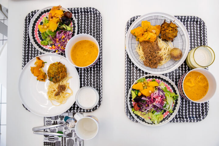 Two trays of healthy vegan meals with salads, pasta, and soup.