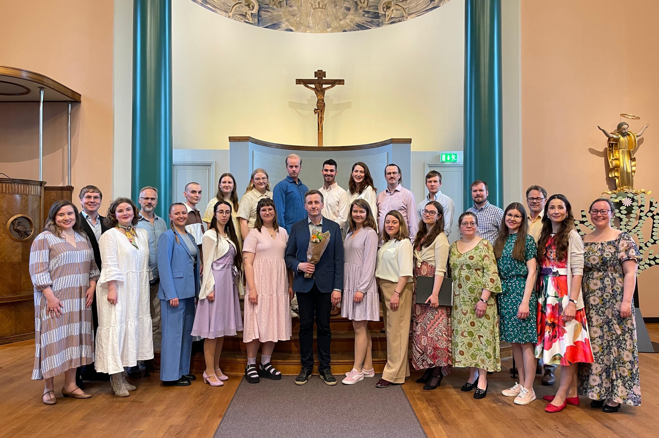 POL kuorolaiset seisoo kahdessa rivissä alttarin edessä keväisissä vaatteissa. Kuoronjohtaja seisoo keskellä.