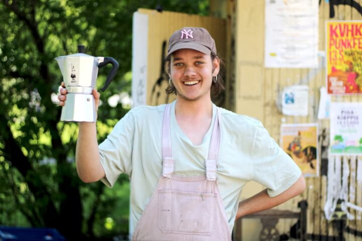 A young man holding coffee by a canopy kiosk in Käpylä neighbourhood in Helsinki.