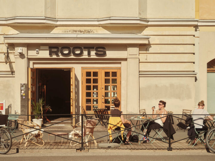 People enjoying coffee and sun outside Roots cafe, with its logo visible.