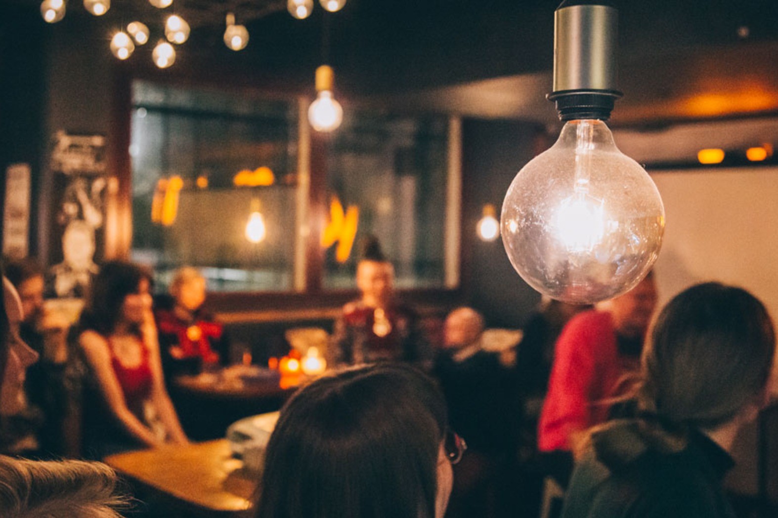 Ihmisiä lämpimästi valaistussa tilassa. Etualalla on hehkulamppu.