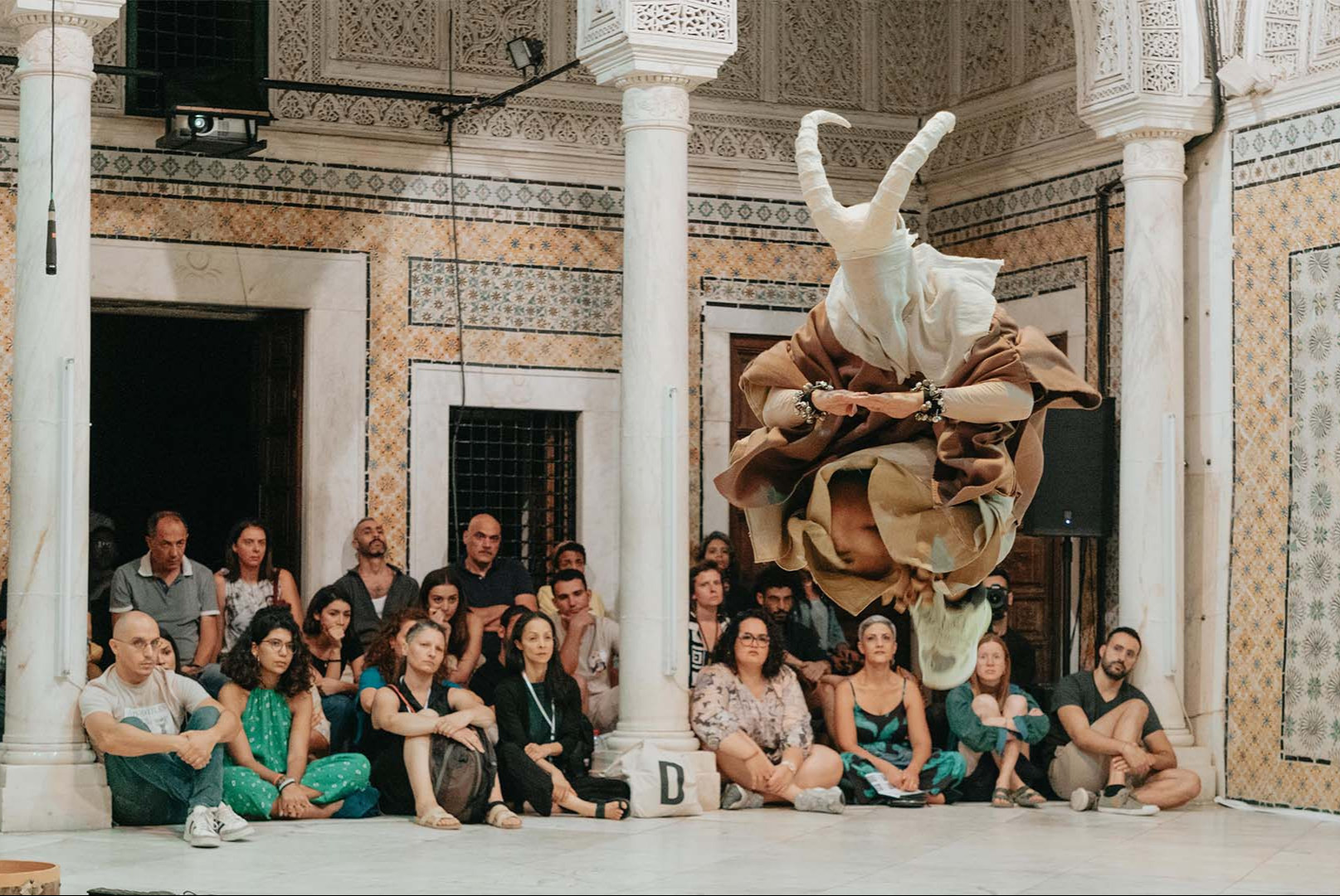 Sarveikkaaseen huppuun pukeutunut tanssija hyppää.