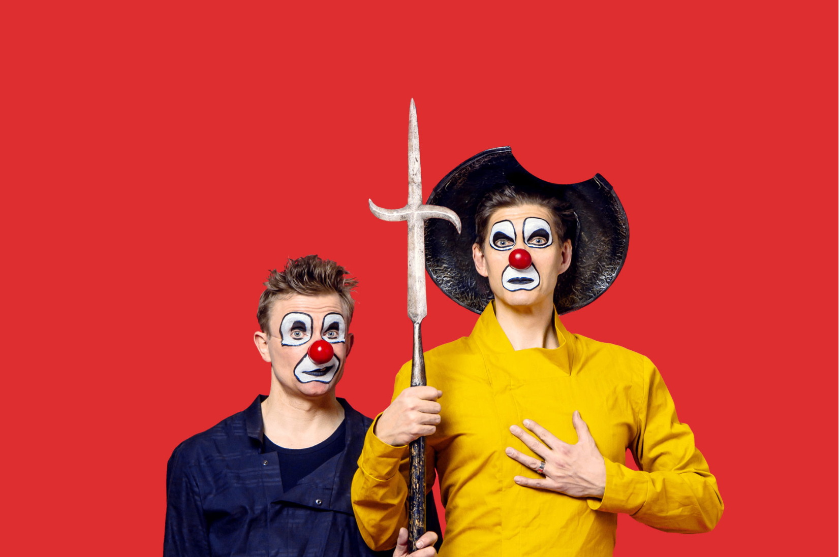 Kaksi klovnia katsovat kameraan, heidän keskellään on peitsi.