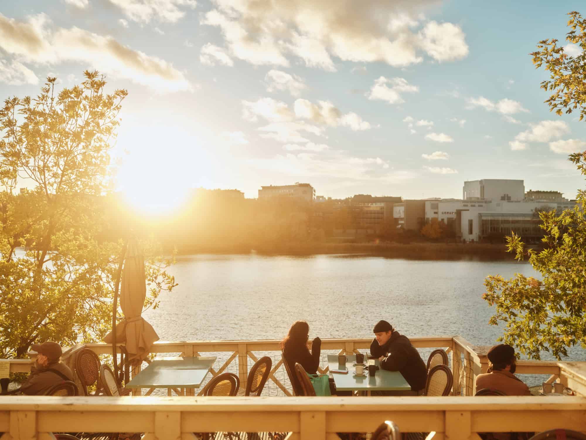 People dining on a patio overlooking a lake at sunset