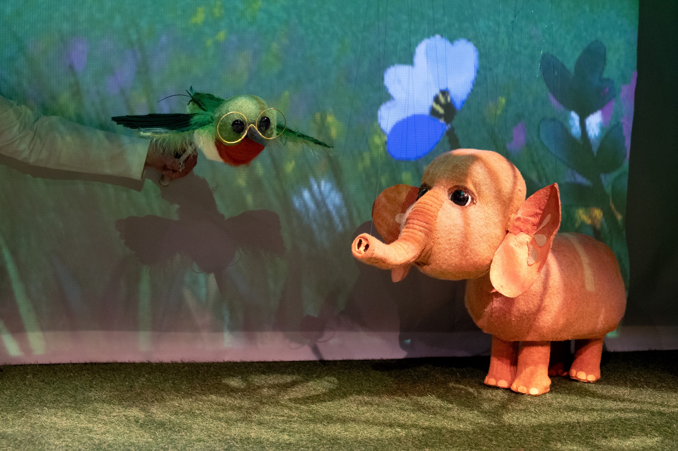 Oranssi Fanni-elefantti ja vihertävä kukkavahtimestari Ari vihreänsävyistä taustaa vasten. Nukketeatterinukkeja.