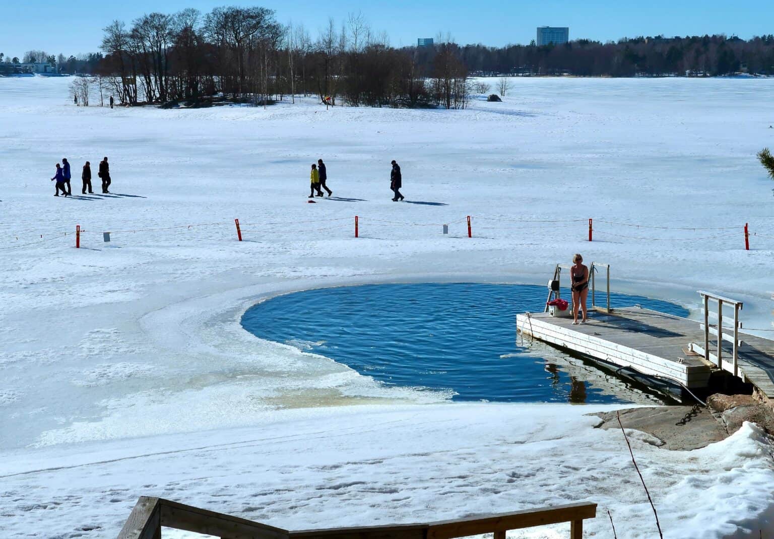 People walking on ice near Seurasaari in Helsinki whilst someone is also ice swimming.
