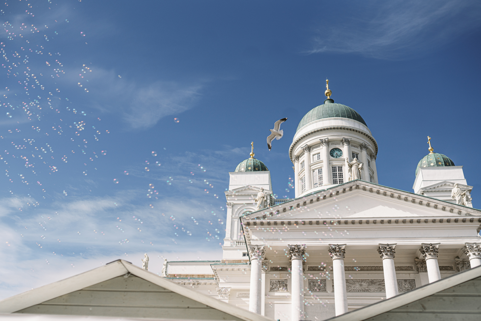 Helsinki Cathedral with bubbles and a seagull against a blue sky.