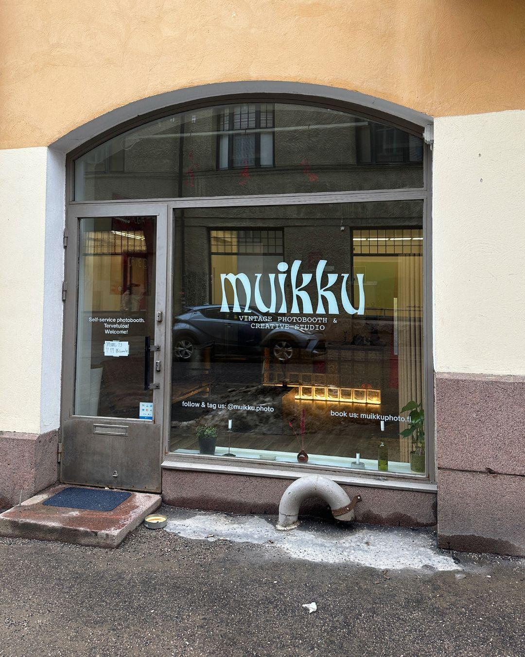 Muikku Photo studio in Helsinki with arched window, logo on glass and warm light inside.