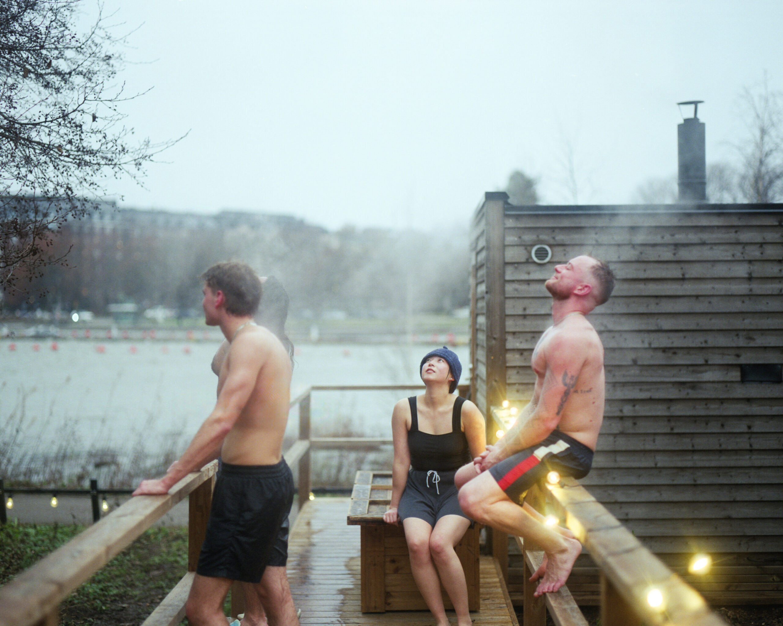 Three happy people sitting outside a sauna, steaming. The background shows snowless Helsinki in November.