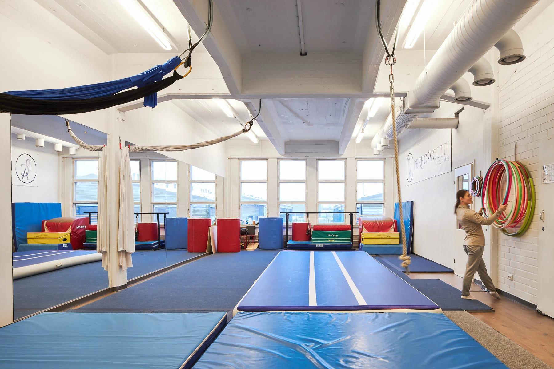 Nainen kuntosalilla pitelee renkaita peilin ja maton edessä.