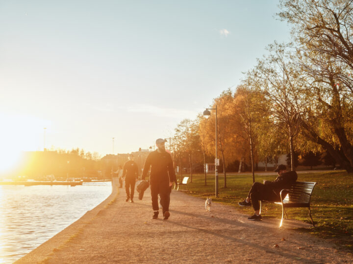 Autumn park scene with people walking and a man resting on a bench at sunset