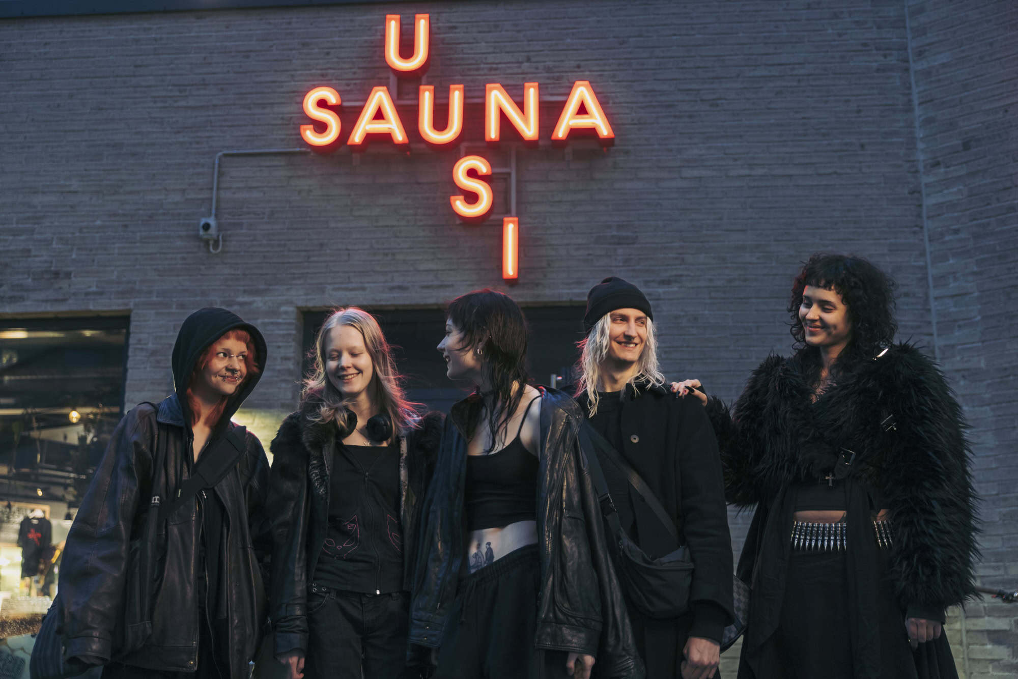 Group of friends in dark clothing in front of "U Saunasi" neon sign