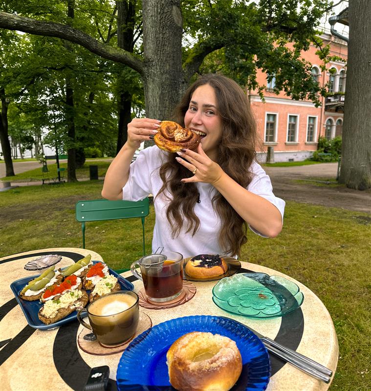 Vrouw eet een kaneelbroodje buiten in een Helsinks park met Fins gebak, koffie en open sandwiches op tafel tijdens een stedentrip