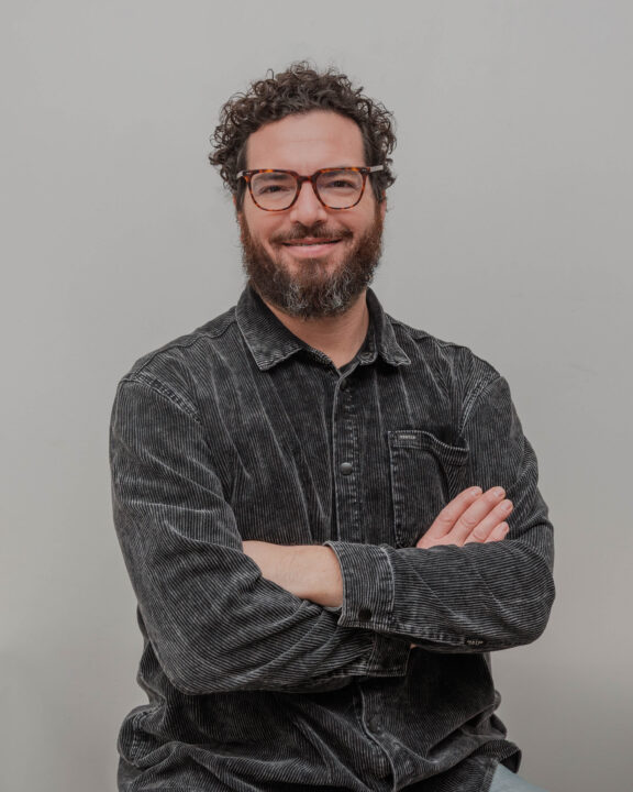 Man with curly hair, beard, and glasses wearing a corduroy shirt